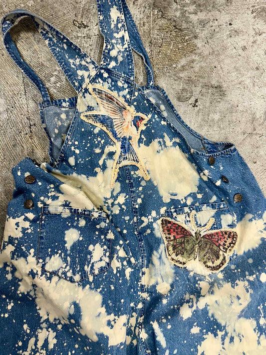 Blue denim overalls with white splatter design and butterfly patches on a textured surface. Boho Chic. Grunge Clothing. Unique Style. 
A Rare Bird Butterfly Overalls
