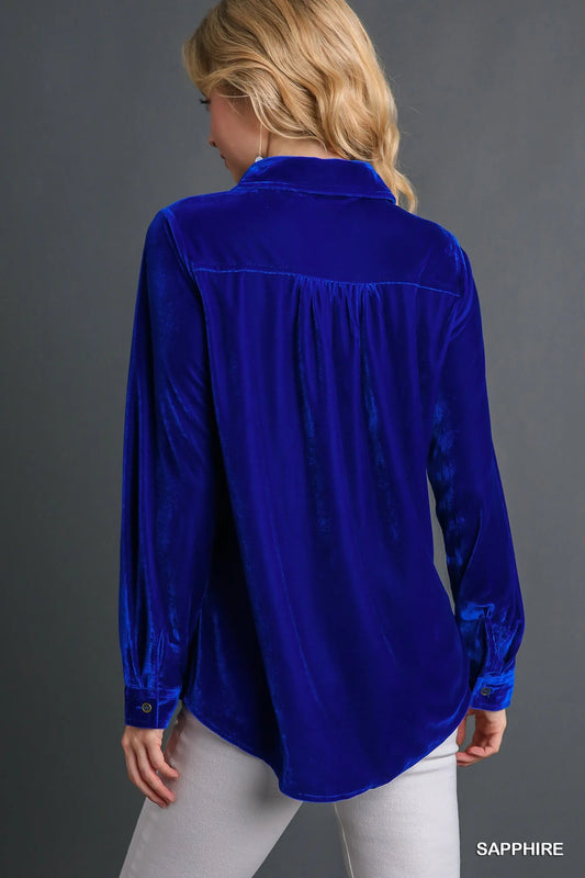 Model wearing a sapphire blue velvet button-down top with wrist cuffs, styled casually with light pants.