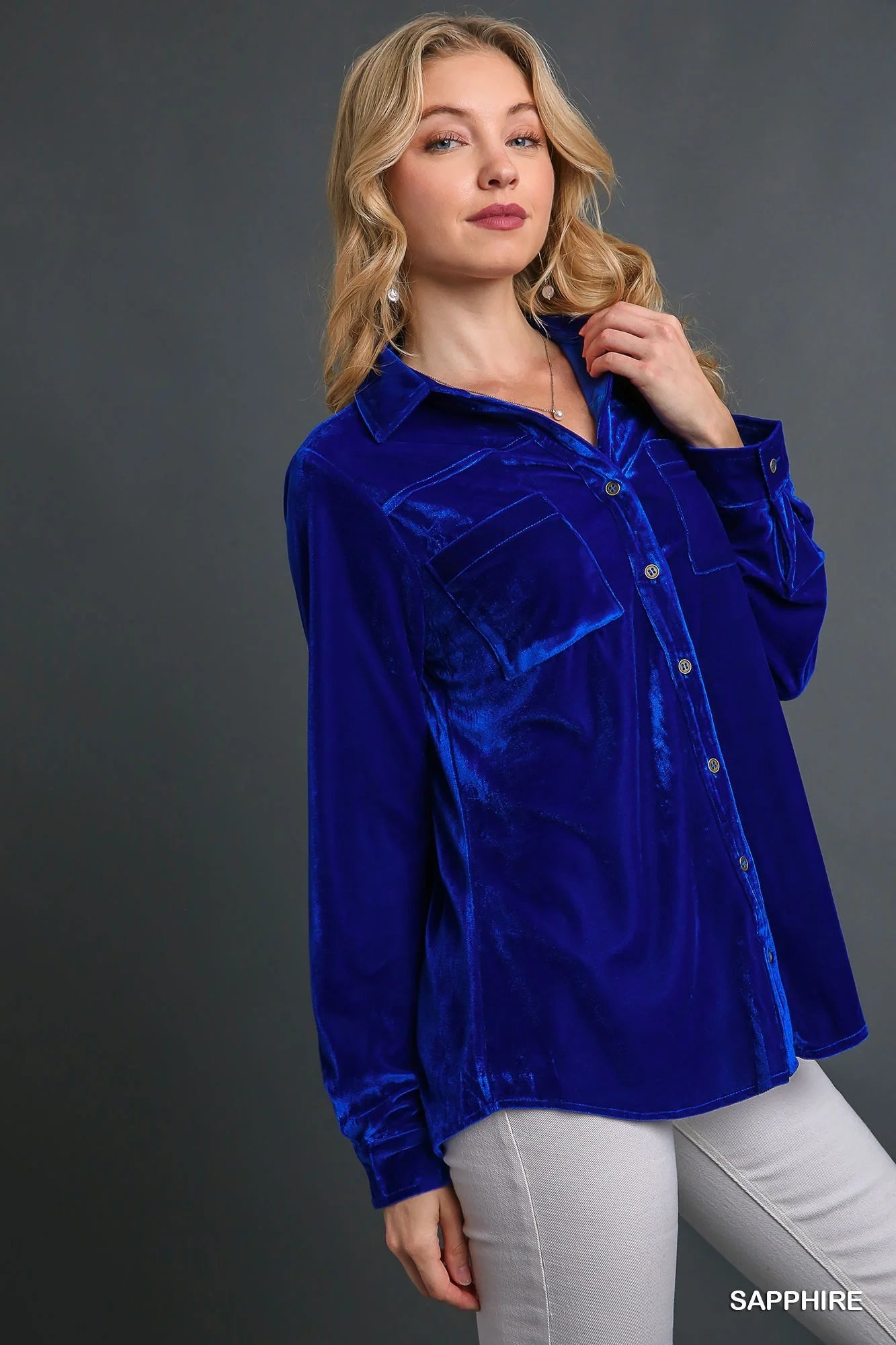 Model wearing a sapphire blue velvet button-down top with wrist cuffs, styled casually with light pants.