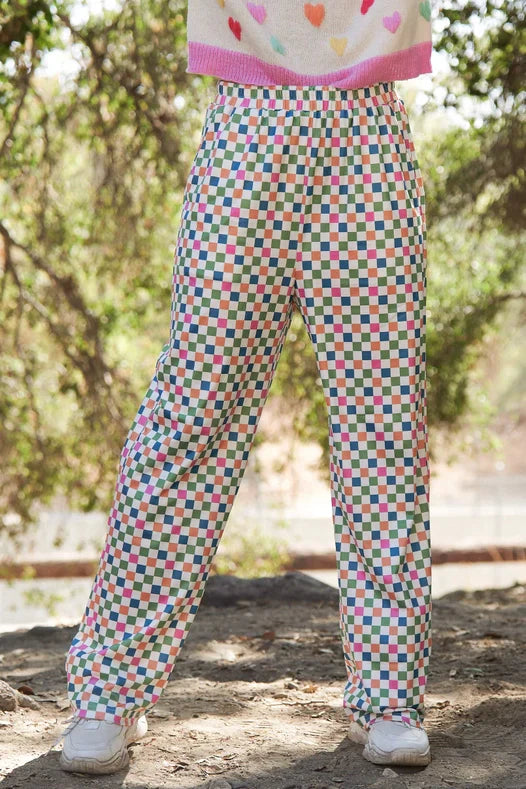 Model wearing colorful checkerboard Just Vibing Pants by J.NNA featuring pink, olive green, blue, and orange checks with a stretchy elastic waistband and wide leg fit.