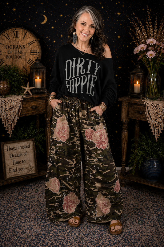 Blue Velvet wide-leg camouflage pants featuring blush floral appliqués, paint splatter detailing, elastic drawstring waist, front and back pockets, and a relaxed boho silhouette.