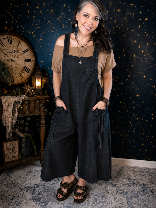 Black cotton wide-leg overalls by Evergreen Guardian featuring adjustable straps, front bib pocket, front pockets, and a relaxed oversized boho silhouette.