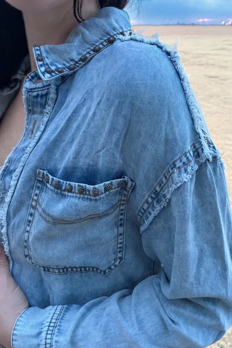 Close-up of Sterling Kreek denim shacket with antiqued stud trim, raw distressed seams and chest pocket