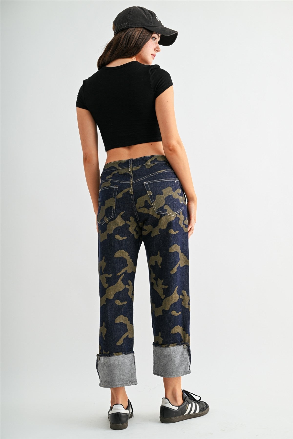 Model wearing stretchy high-rise camo cropped jeans by Mica Denim featuring rolled cuffs, dark wash denim, and olive camouflage print.