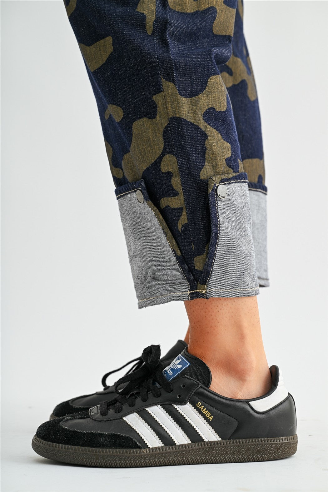 Model wearing stretchy high-rise camo cropped jeans by Mica Denim featuring rolled cuffs, dark wash denim, and olive camouflage print.