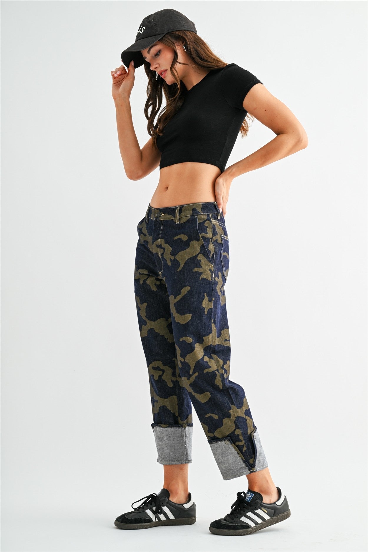 Model wearing stretchy high-rise camo cropped jeans by Mica Denim featuring rolled cuffs, dark wash denim, and olive camouflage print.