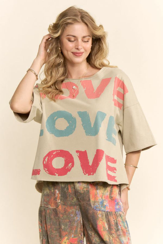 Front: Woman wearing oversized beige graphic tee with colorful LOVE print and relaxed fit
Back: Oversized beige tee with “I love you” written in multiple languages on the back