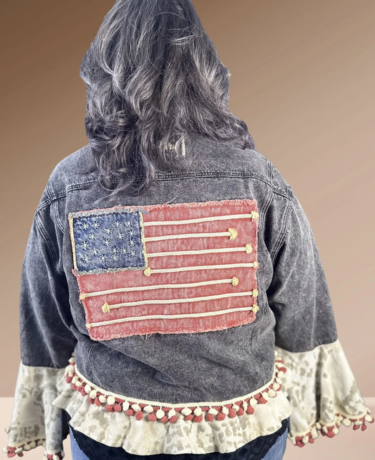Handmade mineral-washed black denim jacket with embroidery, pom details, and bell sleeves by A Rare Bird, one-size fits 4–18.

